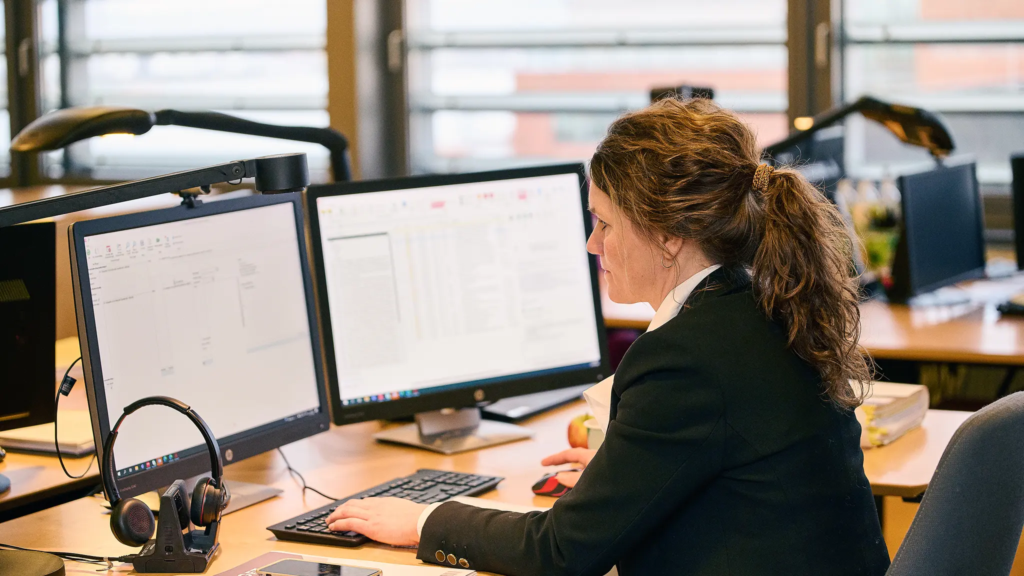 Kvinde ved to computerskærme på kontor